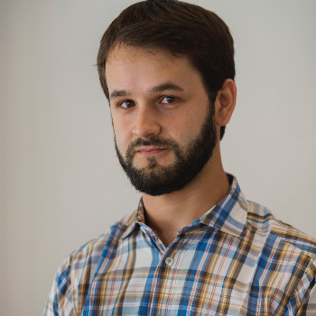 Diogo Bercito, a young white man with brown hair and a full beard and mustache, wearing a plaid brown, tan, and blue button down shirt.